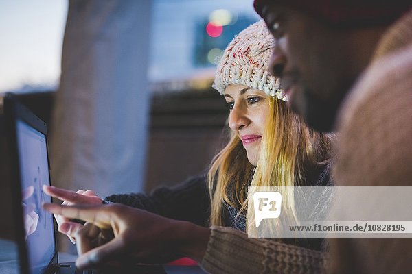 Couple using laptop outdoors at dusk