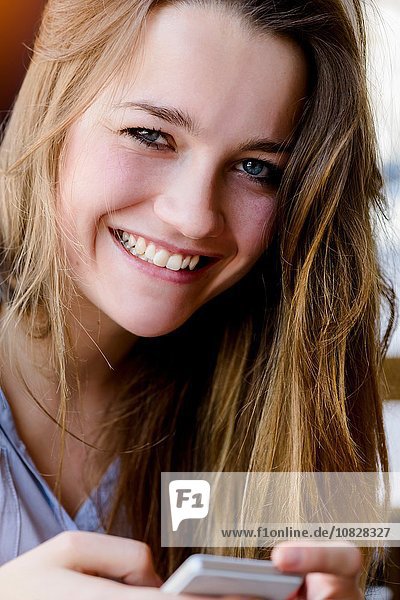 Junge Frau hält Smartphone und schaut lächelnd in die Kamera