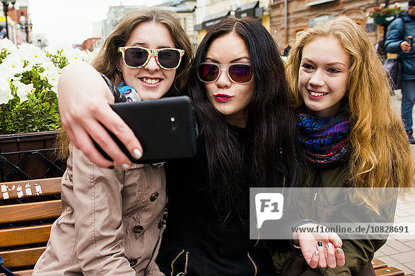 Kaukasische Frauen nehmen Selfie auf Bank