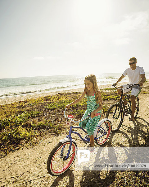 Kaukasischer Vater und Tochter fahren mit dem Fahrrad am Strand