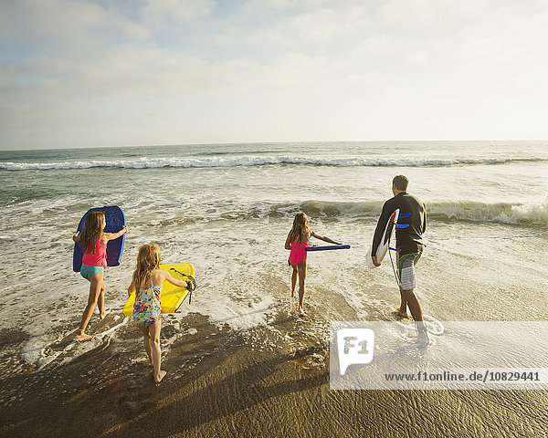 Caucasian father and daughters playing in waves on beach