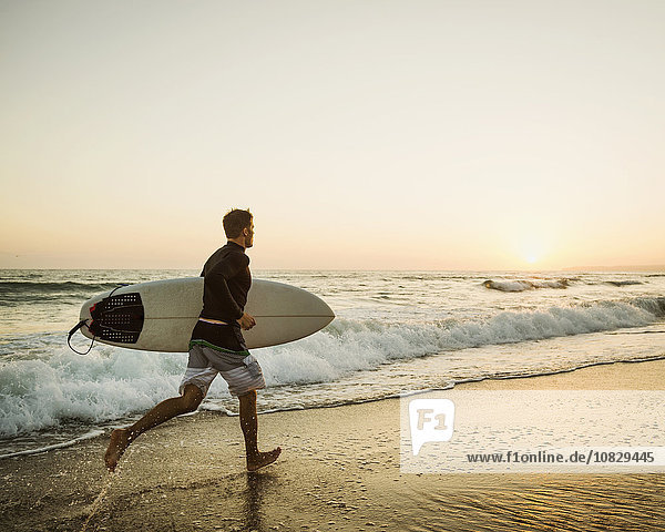 Kaukasischer Mann mit Surfbrett am Strand