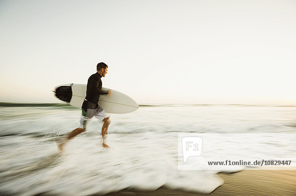 Caucasian man carrying surfboard on beach
