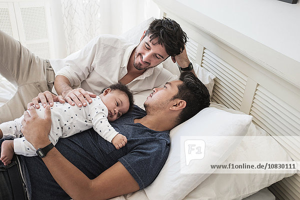 Gay fathers relaxing with baby son on bed