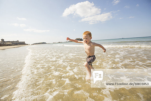 Kaukasischer Junge spielt in den Wellen am Strand