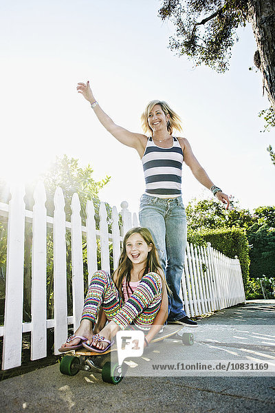 Caucasian mother and daughter riding skateboard on sidewalk