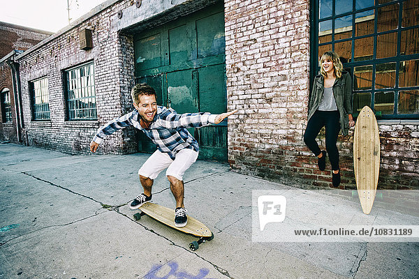 Caucasian couple skateboarding on sidewalk
