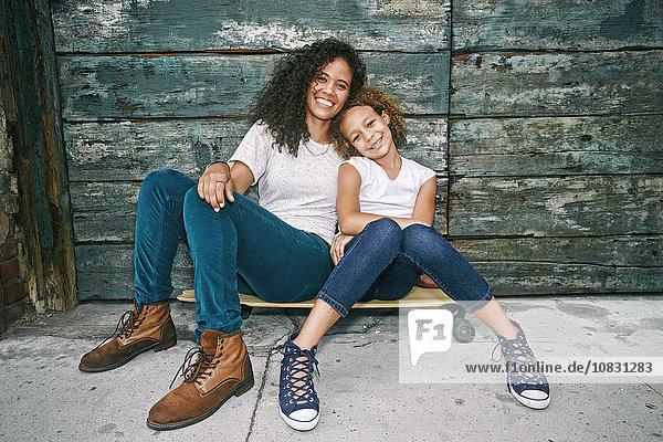 Gemischtrassige Mutter und Tochter sitzen auf einem Skateboard