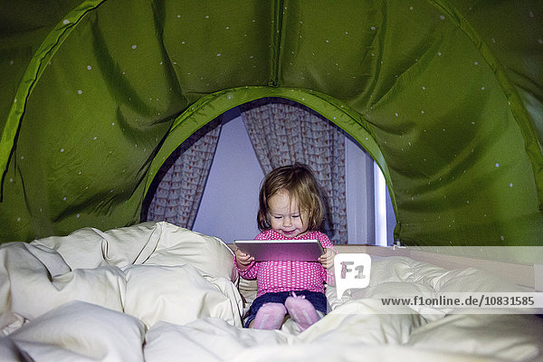 Kaukasisches Baby-Mädchen benutzt digitales Tablet im Zelt