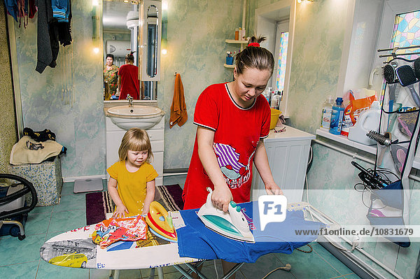 Kaukasische Mutter und Tochter bügeln Wäsche