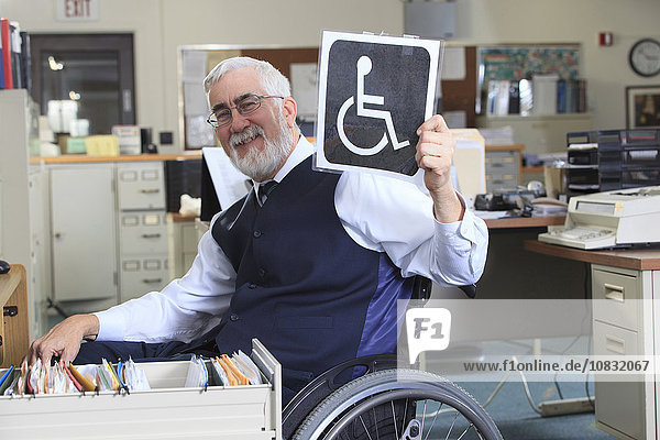 Kaukasischer Geschäftsmann hält Behindertenschild im Büro