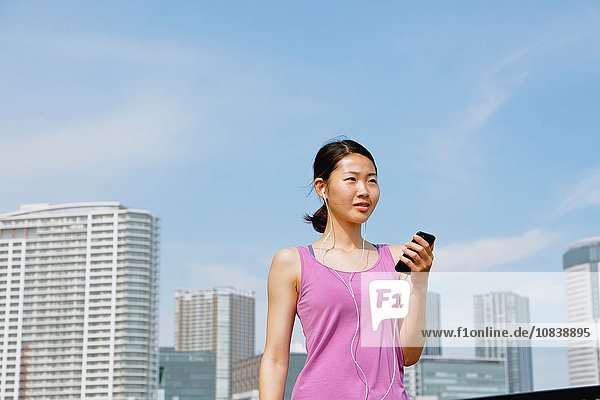 Junge Japanerin mit Smartphone während ihres Laufs in der Innenstadt von Tokio