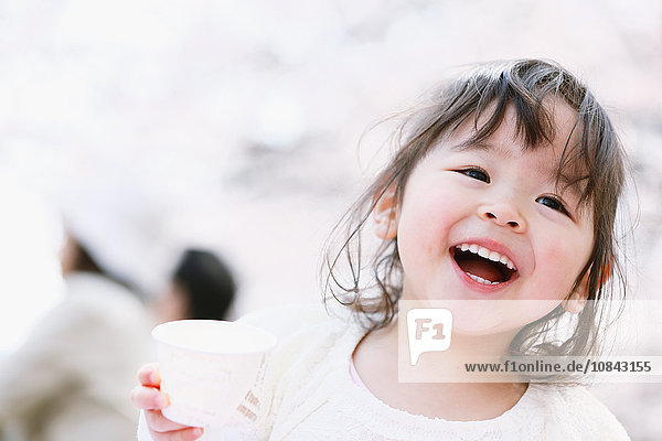 Junges lächelndes japanisches Mädchen genießt die Kirschblüten in einem Stadtpark