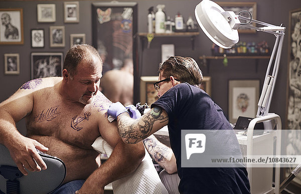 Tattoo artist tattooing man’s shoulder
