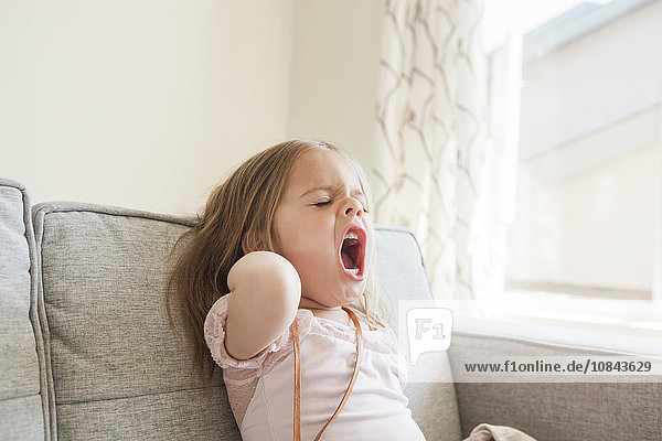 Toddler girl yawning on sofa