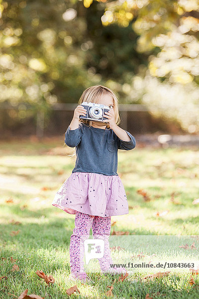 Toddler girl using retro camera in autumn park
