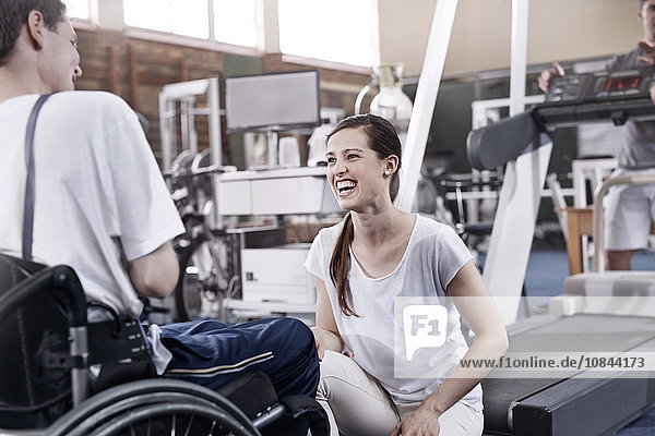 Smiling physical therapist talking to man in wheelchair