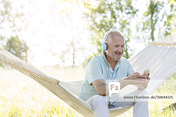 Senior Mann mit Kopfhörer Musik hören mit mp3-Player auf Sommer-Hängematte