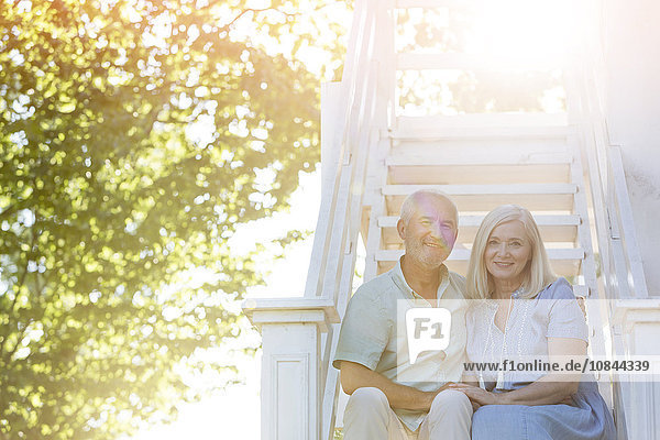 Portrait lächelndes Seniorenpaar auf Sommertreppe sitzend