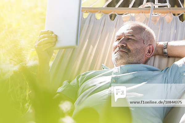 Senioren-Mann mit Digital-Tablett und Entspannung in der Sommer-Hängematte