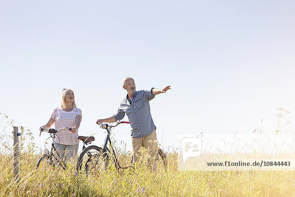 Seniorenpaar Radfahren im sonnigen ländlichen Feld unter blauem Himmel