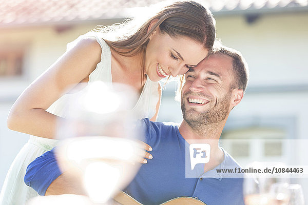 Junges Paar umarmt und lacht auf der Sonnenterrasse