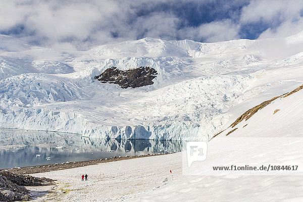 Zwei Wanderer umgeben von eisbedeckten Bergen und Gletschern in Neko Harbor  Antarktis  Polarregionen