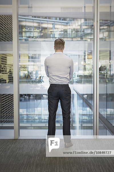 Businessman standing at office window overlooking atrium