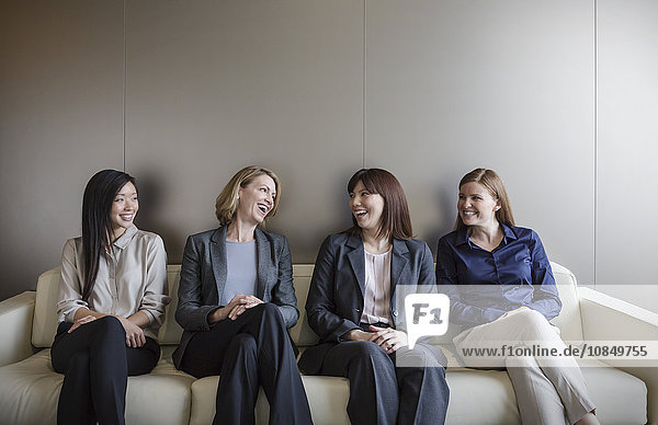 Smiling businesswomen talking in a row on sofa