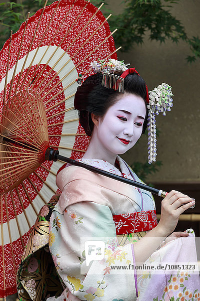 Porträt einer lächelnden Geisha in geblümten Gewändern mit rotem Regenschirm im Sommer  Kyoto  Japan  Asien