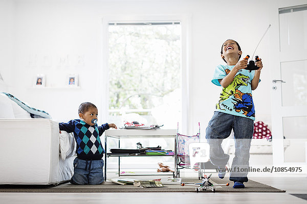 Boy looking at happy brother holding remote of model airplane at home