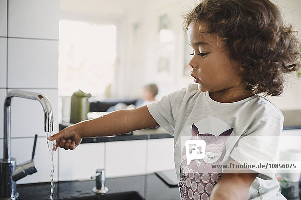 Girl washing hand under faucet in kitchen