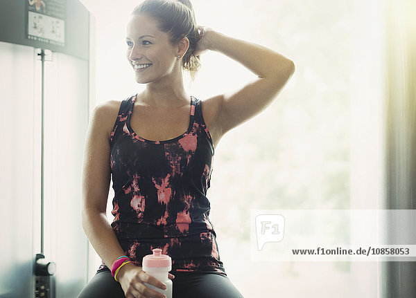 Lächelnde Frau mit Wasserflasche im Fitnessstudio