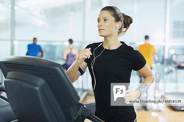 Fokussierte Frau auf dem Laufband mit Kopfhörer im Fitnessstudio