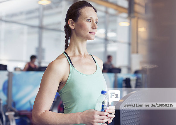 Nachdenkliche Frau trinkt Wasser im Fitnessstudio