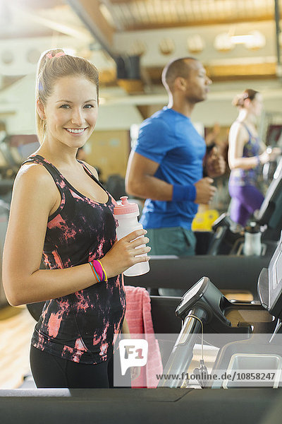 Portrait lächelnde Frau mit Wasserflasche auf dem Laufband im Fitnessstudio