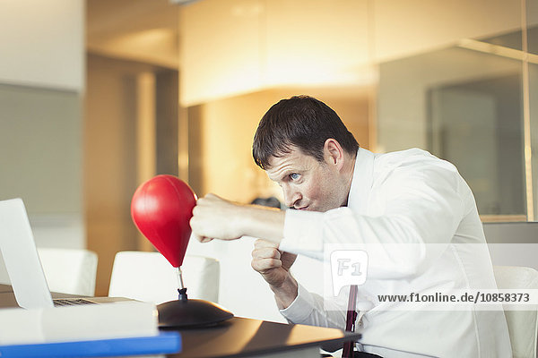 Businessman punching toy punching bag in office