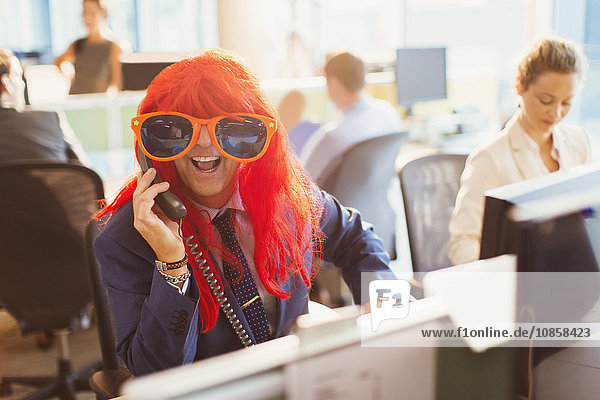 Portrait playful businessman wearing red wig and huge sunglasses in office