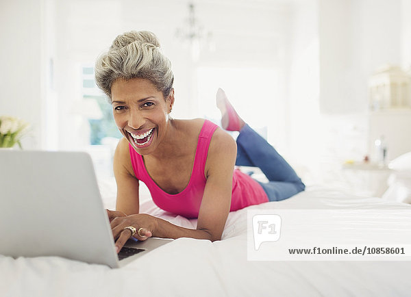 Portrait lachende reife Frau mit Laptop im Bett