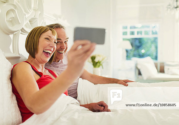 Enthusiastic mature a couple taking selfie in bed