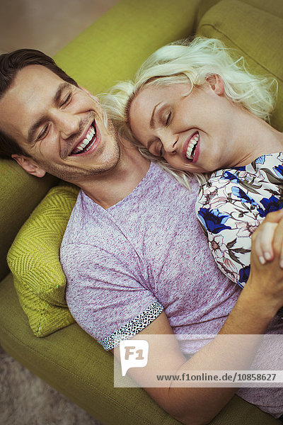 Affectionate laughing couple laying on sofa with eyes closed