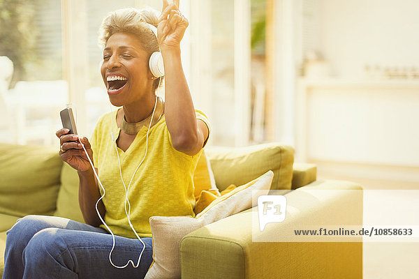 Verspielte reife Frau hört Kopfhörer mit MP3-Player im Wohnzimmer