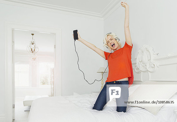 Playful women kneeling on bed listening to music with mp3 player and headphones