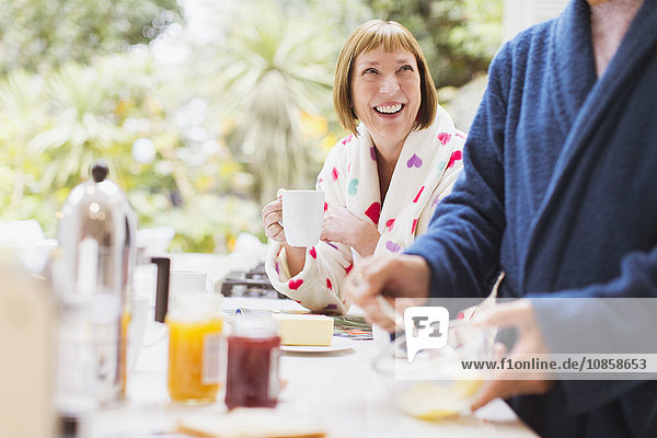 Lächelnde reife Frau beim Kaffeetrinken im Bademantel zum Frühstück
