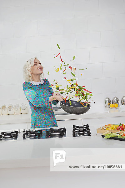 Woman cooking flipping vegetables in skillet in kitchen