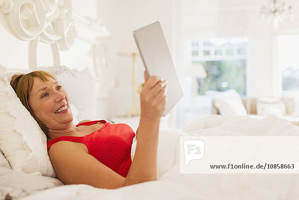 Lächelnde reife Frau mit digitalem Tablett im Bett
