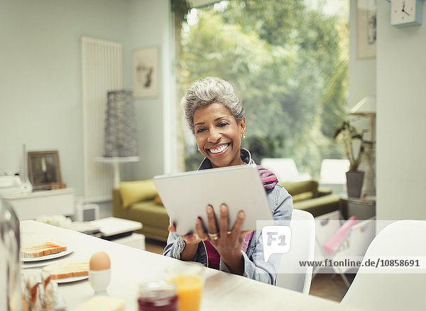 Lächelnde reife Frau mit digitalem Tablett am Frühstückstisch