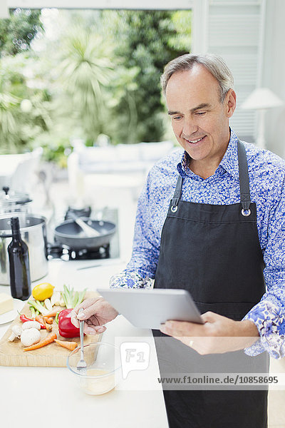 Reifer Mann in der Schürze mit digitalem Tablettenkochen in der Küche