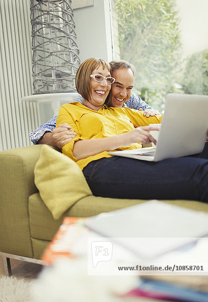 Lächelndes reifes Paar  das sich einen Laptop auf dem Wohnzimmersofa teilt.