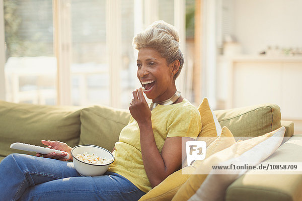 Reife Frau beim Popcornessen und Fernsehen auf dem Wohnzimmersofa